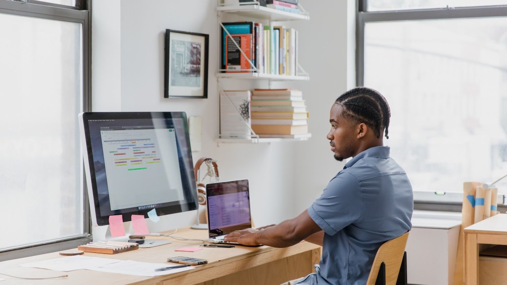 Founder working alone at a desk with a laptop and monitor in a home office, the early days of Ergode